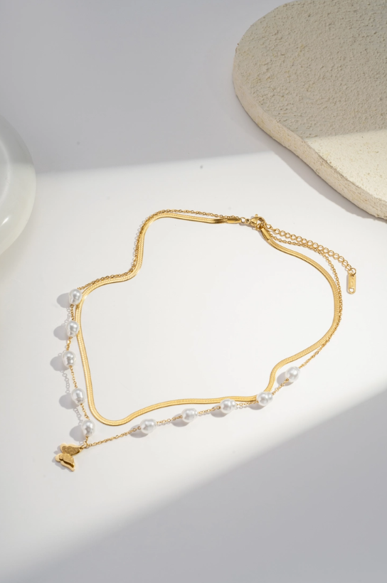 Gold necklace with pearls and butterfly charm on a light background