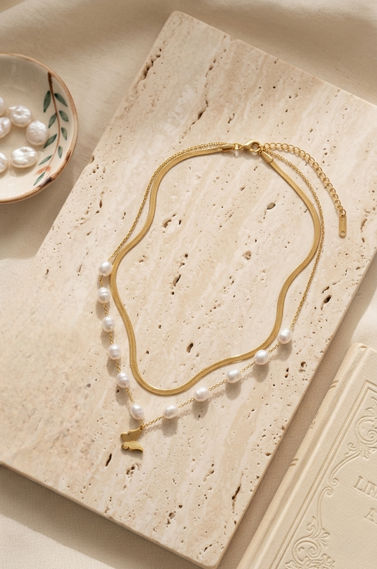 Gold necklace with pearls and butterfly charm on a textured beige surface